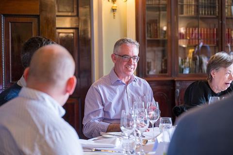 Photograph focused on Anti Fraud Motor Insurers Bureau claims integrity controller John Reynolds at the roundtable, smiling mid-conversation. He wears a lilac striped shirt.